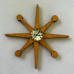 May include: A wooden starburst clock with a small, round clock face at the center. The clock has eight pointed arms with rounded ends. The clock face features black hands and Roman numerals.