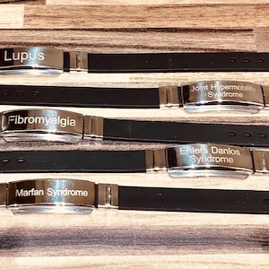 May include: Five silver medical alert bracelets with black silicone bands. The bracelets are engraved with the following medical conditions: Lupus, Joint Hypermobility Syndrome, Fibromyalgia, Ehlers Danlos Syndrome, and Marfan Syndrome.