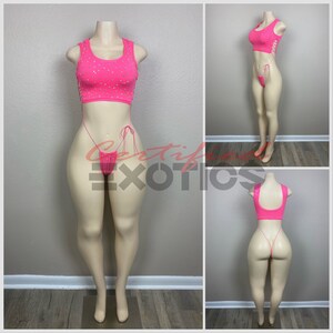 May include: A pink two-piece outfit with rhinestones on the top and a string bottom. The outfit is on a mannequin.