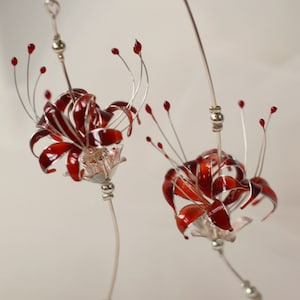 May include: A pair of silver earrings with red flower designs. The flowers are made of wire and have a delicate, intricate design.