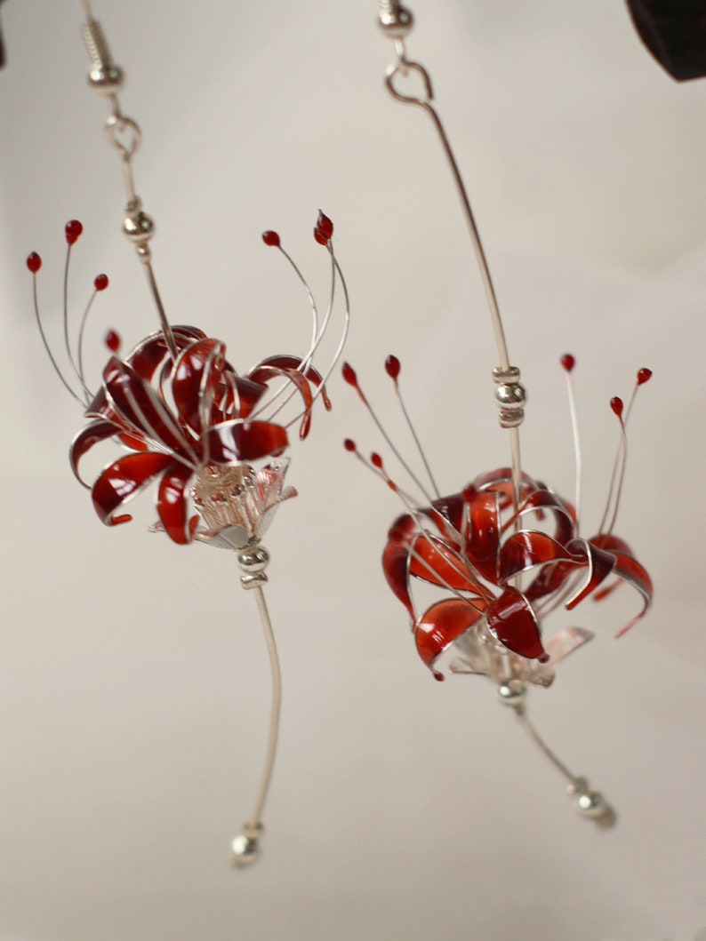 May include: A pair of silver earrings with red flower designs. The flowers are made of wire and have a delicate, intricate design.