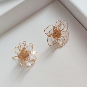 May include: A pair of gold flower-shaped earrings with clear plastic petals. The earrings are delicate and feminine.