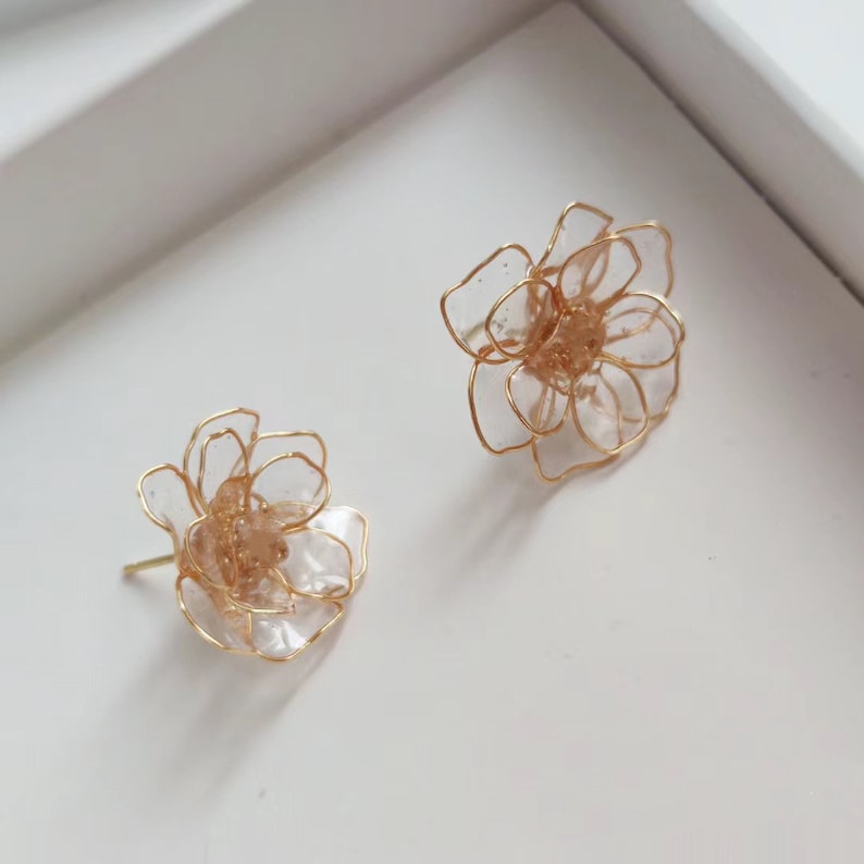 May include: A pair of gold flower-shaped earrings with clear plastic petals. The earrings are delicate and feminine.
