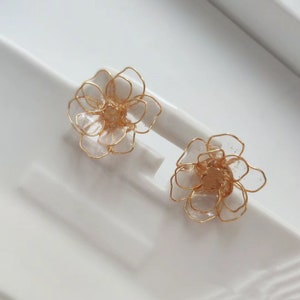May include: A pair of gold flower-shaped earrings with clear plastic petals.