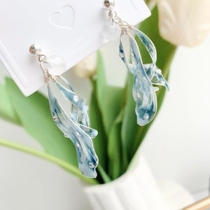 May include: A pair of silver dangle earrings with blue and white accents. The earrings feature a delicate, flowing design with a clear crystal bead at the top.