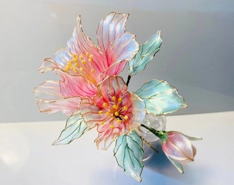 May include: A delicate pink and blue flower made of wire and translucent plastic. The flower has a gold wire outline and is in a clear vase.
