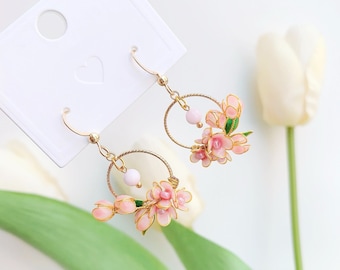 May include: A pair of gold hoop earrings with pink flower accents. The earrings are delicate and feminine, and would be a great addition to any jewelry collection.
