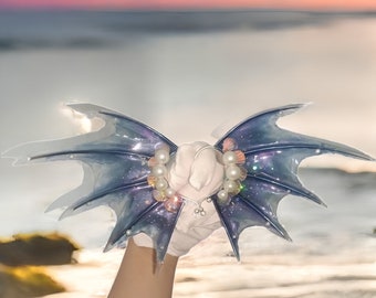 May include: A pair of iridescent blue wings with pearl and shell accents. The wings are held in a hand with white gloves.