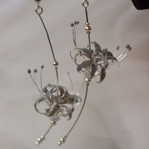 May include: A pair of silver earrings featuring delicate, detailed flower designs. The flowers are made of wire and have a slightly textured finish.