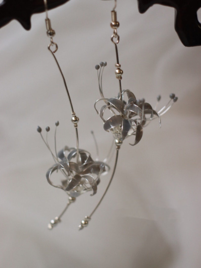 May include: A pair of silver earrings featuring delicate, detailed flower designs. The flowers are made of wire and have a slightly textured finish.