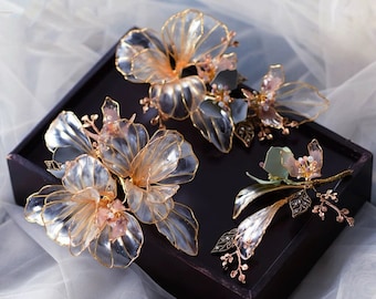 May include: Three gold and clear floral hair clips with delicate details. The clips are arranged on a black surface.