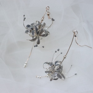 May include: A pair of silver earrings with a delicate flower design. The earrings are made of wire and have small silver beads.