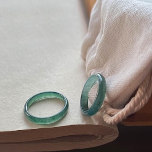 May include: Two green jade rings on a white surface. The rings are smooth and have a polished finish.