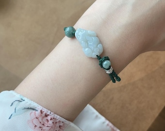 May include: A green string bracelet with a white jade charm in the shape of a cloud. The charm has a silver bead on the bottom.