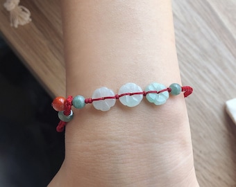 May include: A red string bracelet with green and white jade beads. The beads are carved with a flower design.