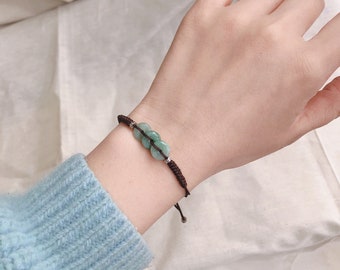 May include: A brown string bracelet with three green jade beads. The beads are round and have a smooth surface.
