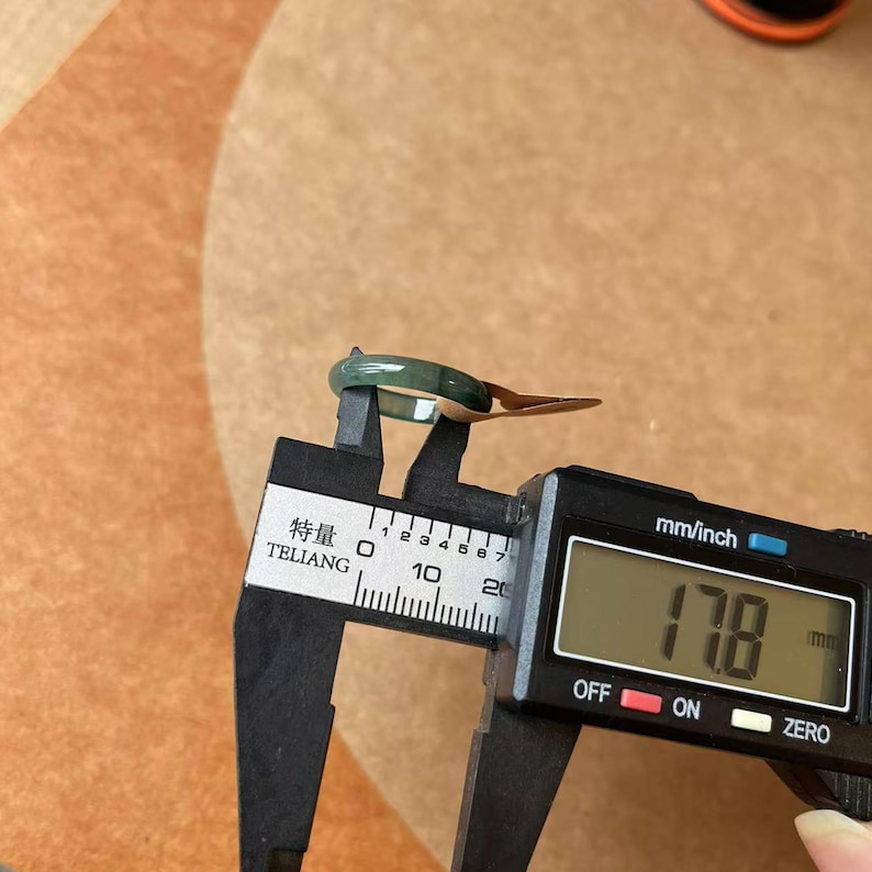 May include: A green jade ring being measured with a digital caliper. The caliper reads 17.8 mm.