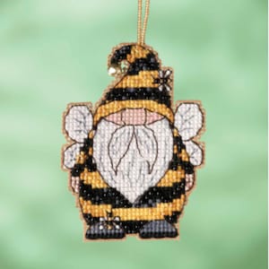 Pode incluir: Um ornamento de gnomo com tema de abelha com um corpo listrado amarelo e preto, barba branca e um chapéu amarelo com listras pretas e uma pequena flor. O gnomo tem asas e está segurando uma pequena abelha.