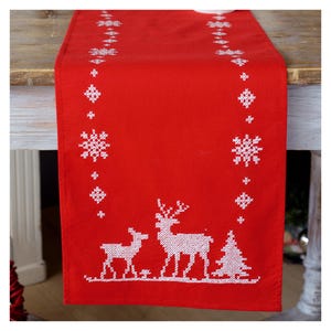 May include: A red Christmas table runner featuring white embroidered snowflakes, reindeer, and a Christmas tree. The runner is made of a soft fabric, ideal for festive decor. The runner is approximately 152 cm long.