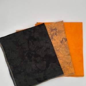 Puede incluir: Tres cuadrados de tela, uno negro con un patrón moteado, uno naranja con un patrón moteado y uno naranja sólido.