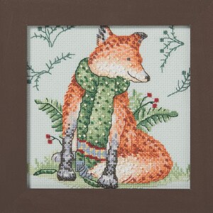 Könnte beinhalten: Ein gerahmtes Kreuzstich-Stickbild, das einen orangefarbenen Fuchs mit einem grünen, gepunkteten Schal zeigt. Der Fuchs ist vor einem hellblauen Hintergrund mit grünem Farnlaub und kleinen roten Beeren dargestellt, eingefasst in einen dunkelbraunen Rahmen.