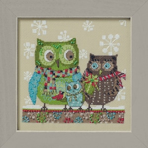 Puede incluir: Obra de arte de punto de cruz de tres búhos con bufandas, sobre un fondo de copos de nieve. Los búhos son de tonos verdes, azules y marrones, con detalles intrincados. La obra está enmarcada en un marco gris claro.