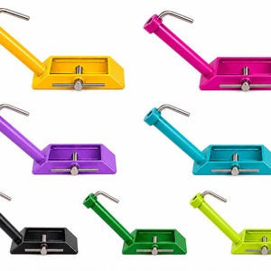 Könnte beinhalten: Eine Sammlung von sieben Fliegenbindestöcken aus Metall in Gelb, Pink, Lila, Türkis, Schwarz, Dunkelgrün und Hellgrün. Jeder Bindestock verfügt über eine rechteckige Basis mit einer zentralen Spannschraube und einen abgewinkelten Arm mit einer Metallklemme.