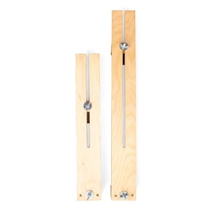 May include: Two wooden leatherworking tools. The tools are made of light-colored wood with a long, rectangular shape. Each tool has a metal screw and a slot down the center. One tool is shorter than the other.