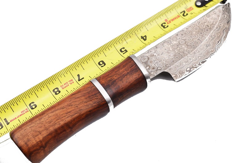 May include: A brown wooden handled knife with a silver blade. The blade has a patterned finish. The knife is measured against a yellow tape measure, showing it is 8 inches long.