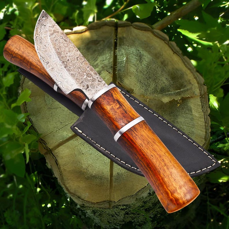 May include: A Damascus steel hunting knife with a wooden handle and a leather sheath. The knife has a decorative pattern on the blade and a silver metal band around the handle.