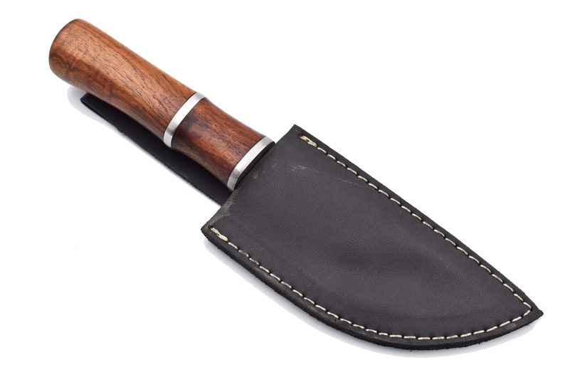 May include: A brown wooden handled knife with a black leather sheath. The sheath has white stitching around the edges.