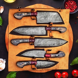 May include: A set of five kitchen knives with wooden handles and Damascus steel blades, displayed in a brown leather roll with individual slots for each knife.
