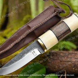 May include: A handcrafted knife with a wooden and bone handle, a silver blade, and a brown leather sheath. The knife has a rustic, outdoorsy aesthetic, suitable for camping or hunting. The blade has the text "TBP".