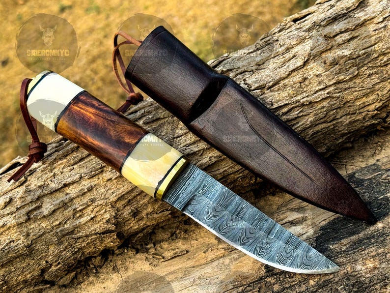 May include: A Damascus steel knife with a wooden handle and leather sheath. The handle features a combination of dark wood, bone, and brass accents. The sheath is dark brown leather. The knife is designed for outdoor use.