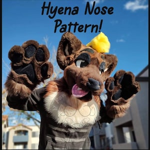 May include: A hyena-themed costume head and paws, with the text "Hyena Nose Pattern!" The head is brown with black accents, a pink tongue, and a yellow tuft of hair. The paws are brown with black paw pads. The costume is worn outdoors.