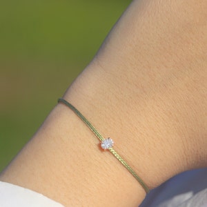 Op de afbeelding: Een groene armband van touw met een klein, helder, ovaalvormig edelsteentje.