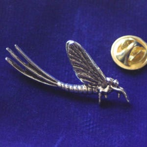 Puede incluir: Pin de metal plateado de un insecto efímero con un cierre de pin dorado.