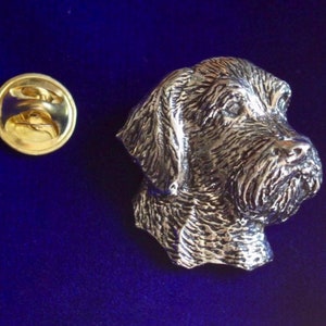 Peut inclure: Une épingle en métal argenté représentant la tête d'un Braque allemand à poil dur. L'épingle est détaillée, avec un design texturé, et est fixée à un dos d'épingle doré.