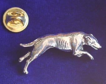 以下が含まれることがあります： 走るポーズをとったグレーハウンド犬の形をした銀色の金属製ラペルピンで、筋肉質な体と細い尻尾が詳細に表現されています。ピンには、中央にポストが付いた円形の金色の金属製クラッチバック留め具が付属しています。