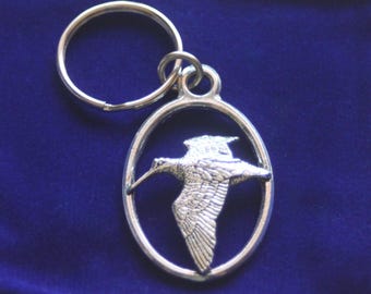 Puede incluir: Llavero de plata con un anillo circular y un dije ovalado con un recorte detallado de un pájaro en vuelo.