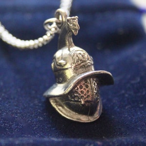 May include: Silver pendant necklace featuring a detailed replica of a Roman gladiator helmet. The helmet is silver with a textured design and a raised face.