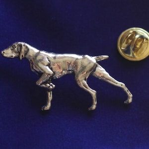 Può includere: Uno spillo a forma di Bracco tedesco a pelo corto di colore argento. Lo spillo è in posizione di corsa e ha un retro dello spillo di colore dorato.