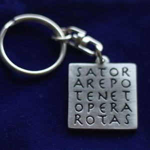 Può includere: Portachiavi in ​​argento con un ciondolo quadrato che presenta il quadrato di parole latino "SATOR AREPO TENET OPERA ROTAS".