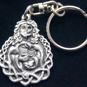 May include: Silver-toned keychain featuring a Celtic knot design with a detailed image of a woman holding a skeleton.
