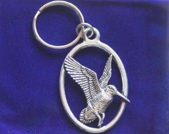 Puede incluir: Llavero de plata con un diseño de pájaro plateado detallado en un marco ovalado. El pájaro está en vuelo con las alas extendidas.