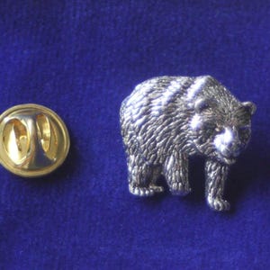Könnte beinhalten: Silberfarbener Bären-Pin mit detaillierter, strukturierter Oberfläche. Der Pin hat eine goldfarbene Rückseite mit einem Sicherheitsverschluss.