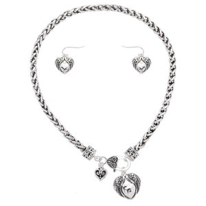 May include: Silver necklace and earrings set with a braided chain and heart pendant with angel wings. The pendant has a smaller heart charm attached.