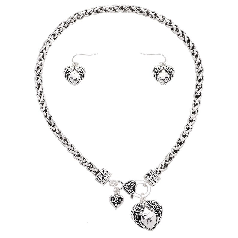 May include: Silver necklace and earrings set with a braided chain and heart pendant with angel wings. The pendant has a smaller heart charm attached.