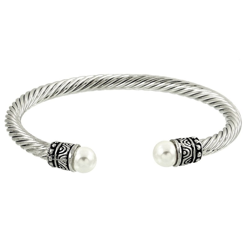 Puede incluir: Un brazalete de plata con un dise&ntilde;o trenzado y dos acentos de perlas blancas. Los extremos del brazalete est&aacute;n adornados con intrincados acentos de patrones negros y plateados.