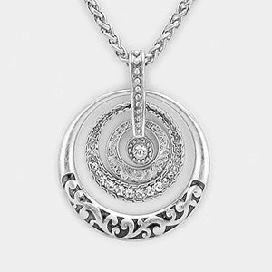 Puede incluir: Collar de plata con un colgante circular que presenta tres c&iacute;rculos conc&eacute;ntricos con un cristal en el centro. El c&iacute;rculo exterior tiene un dise&ntilde;o floral decorativo.